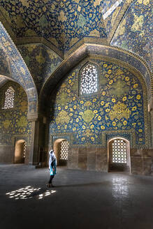 Seitenansicht einer muslimischen Frau in einer majestätischen iranischen Moschee mit ornamentalen Wänden, die mit bunten Mosaiken und Glasfenstern bedeckt sind - ADSF15264