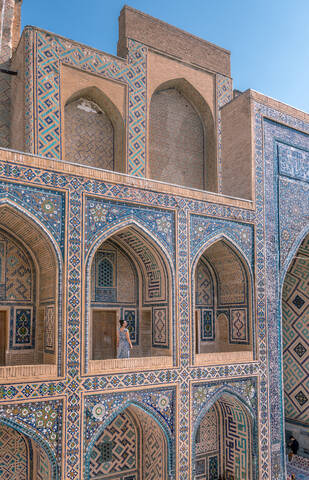 Female traveler walking on terrace of arched Islamic building with blue ornaments while visiting Registan in Samarkand, Uzbekistan stock photo