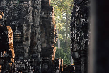 Ancient stone monument with face sculptures in wall illuminated with sunlight, Thailand - ADSF15279