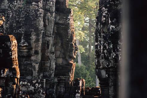 Antikes Steindenkmal mit Gesichtsskulpturen in einer vom Sonnenlicht beleuchteten Wand, Thailand - ADSF15279