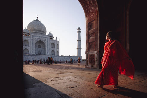 India - November 9, 2012: Indian female in traditional dress standing barefoot on square and admiring amazing view of Taj Mahal - ADSF15298