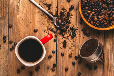 Draufsicht auf ein köstliches Getränk in einem Becher auf dem Tisch mit Kaffeebohnen und gemahlenem Kaffee in einem Metallfilter - ADSF15309