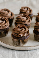 Appetitliche süße Schokoladen-Cupcakes mit Schokoladenbuttercreme, serviert auf einem runden Tablett auf dem Tisch - ADSF15315