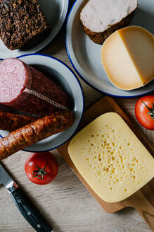 Draufsicht auf köstlichen Käse und Salami auf einem Tisch mit reifen Tomaten und Vollkornbrot in der Küche - ADSF15321