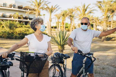 Senior couple with face mask walking with cycle at park - MPPF01080