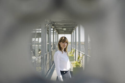 Confident businesswoman standing in greenhouse seen through metal stock photo