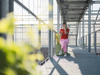 Businesswoman talking over smart phone while sitting on footbridge in greenhouse - JOSEF01631