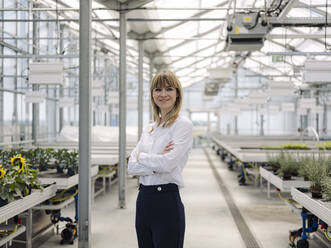 Smiling businesswoman with arms crossed standing in greenhouse - JOSEF01637