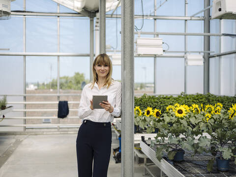 Smiling businesswoman using digital tablet while standing by plants in greenhouse stock photo