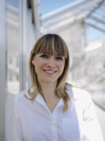 Close-up of smiling businesswoman with blond hair standing by wall stock photo