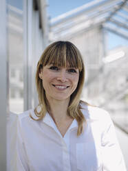 Close-up of smiling businesswoman with blond hair standing by wall - JOSEF01667