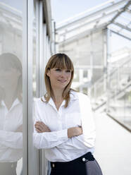 Thoughtful businesswoman with arms crossed standing by wall at greenhouse - JOSEF01668