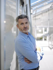 Confident businessman with arms crossed standing by wall at greenhouse - JOSEF01669