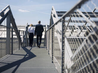 Colleagues discussing while walking on footbridge during sunny day - JOSEF01682