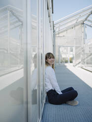 Smiling businesswoman sitting on floor at greenhouse - JOSEF01683