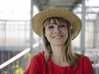 Close-up of smiling businesswoman wearing hat in greenhouse - JOSEF01708