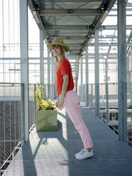 Businesswoman wearing hat dancing on footbridge in greenhouse - JOSEF01709