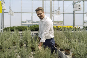 Smiling male entrepreneur examining potted plants in nursery - JOSEF01748