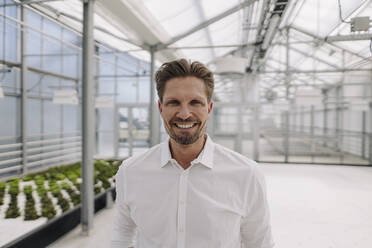 Smiling male owner standing in greenhouse - JOSEF01761