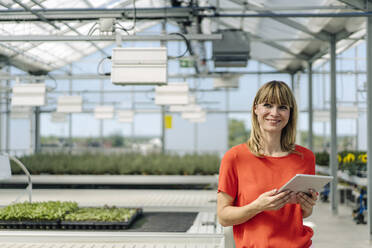 Lächelnde Unternehmerin, die ein digitales Tablet benutzt, während sie in einer Gärtnerei steht - JOSEF01764