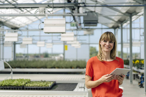 Lächelnde Unternehmerin, die ein digitales Tablet benutzt, während sie in einer Gärtnerei steht - JOSEF01764