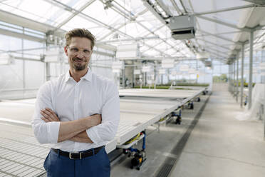 Male professional with arms crossed standing in greenhouse - JOSEF01783