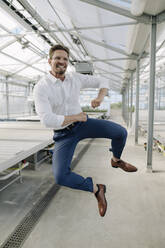 Cheerful businessman jumping in greenhouse - JOSEF01785