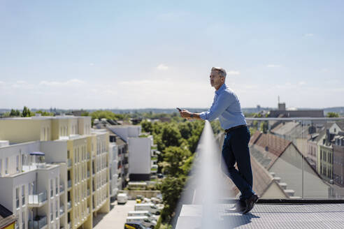 Nachdenklicher Geschäftsmann steht am Geländer eines Balkons gegen den Himmel an einem sonnigen Tag - JOSEF01806