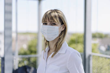 Close-up of female entrepreneur wearing mask standing in greenhouse - JOSEF01817