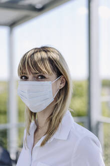 Close-up of female entrepreneur wearing mask working in greenhouse - JOSEF01818