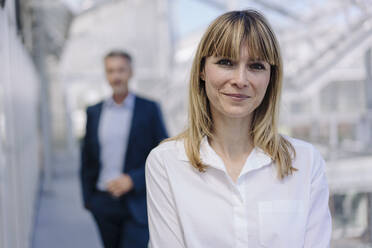 Close-up of smiling businesswoman with male coworker in background at greenhouse - JOSEF01821