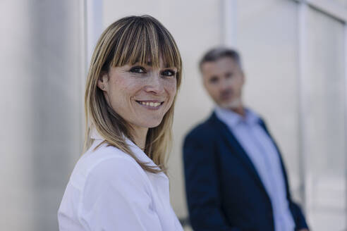 Smiling female professional with businessman standing against wall in greenhouse - JOSEF01825