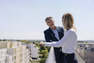 Geschäftsleute, die auf einem Balkon gegen den klaren Himmel diskutieren - JOSEF01829