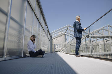 Male and female coworkers talking over smart phone on footbridge in greenhouse - JOSEF01836