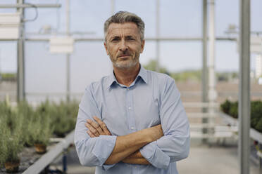 Confident male professional with arms crossed standing in plant nursery - JOSEF01841