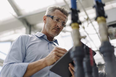 Male professional wearing eyewear using digital tablet while standing in greenhouse - JOSEF01856