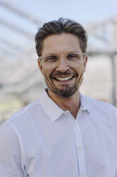 Close-up of smiling male professional wearing eyeglasses in plant nursery - JOSEF01865