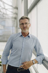 Handsome male professional standing by window in greenhouse - JOSEF01880