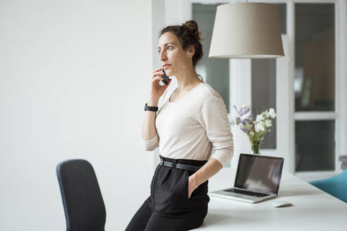 Weibliche Unternehmerin, die am Tisch stehend über ein Mobiltelefon spricht - JOSEF01905