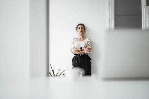 Serious businesswoman with arms crossed standing against white wall stock photo