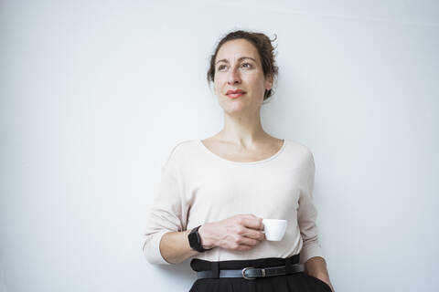 Thoughtful businesswoman holding coffee cup standing against white wall stock photo