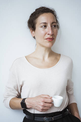 Nachdenkliche Unternehmerin mit Kaffeetasse an einer weißen Wand stehend, lizenzfreies Stockfoto