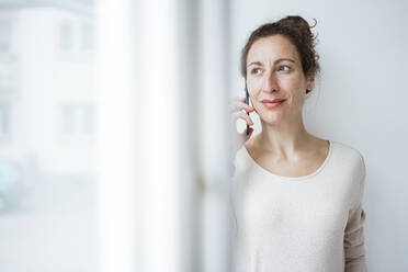 Geschäftsfrau, die über ein Mobiltelefon spricht, gesehen durch ein Fenster - JOSEF01915