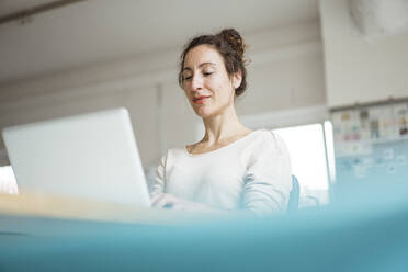 Smiling female entrepreneur working over laptop - JOSEF01920