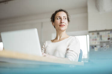 Thoughtful female entrepreneur with laptop on table - JOSEF01921