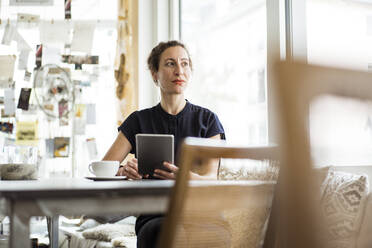 Thoughtful female owner with coffee on table using digital tablet in restaurant - JOSEF01923