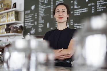 Confident female owner standing against blackboard in coffee shop - JOSEF01927