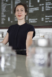 Female owner standing at counter against blackboard in restaurant - JOSEF01928