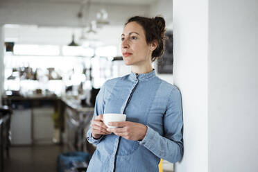 Nachdenkliche Geschäftsfrau mit Kaffeetasse an der Wand eines Cafés - JOSEF01936