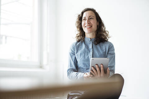 Smiling businesswoman using digital tablet while sitting against wall stock photo
